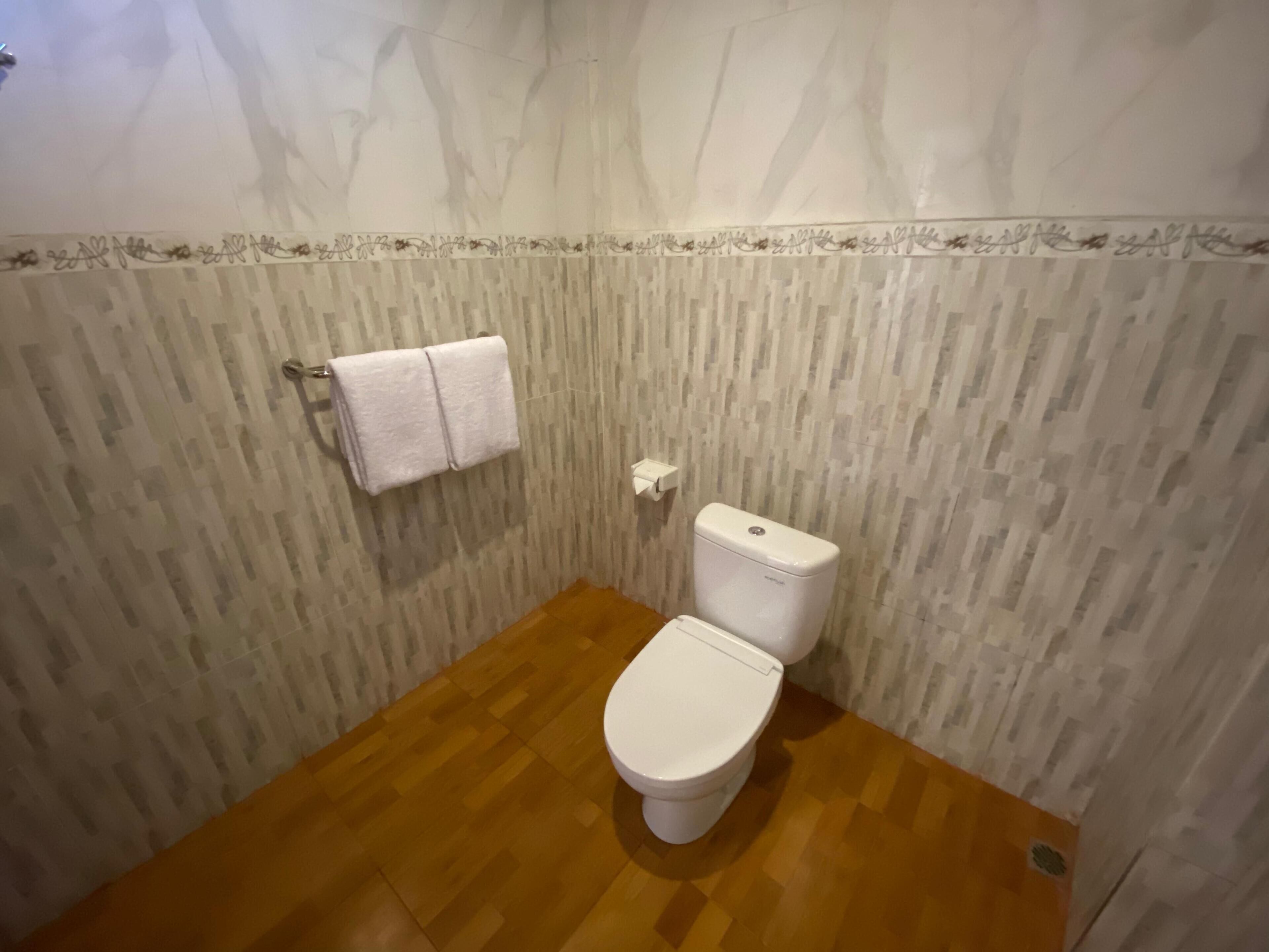Ein kleines Badezimmer mit Toilette in Weiß, Holzboden und Wandverkleidung mit Muster.