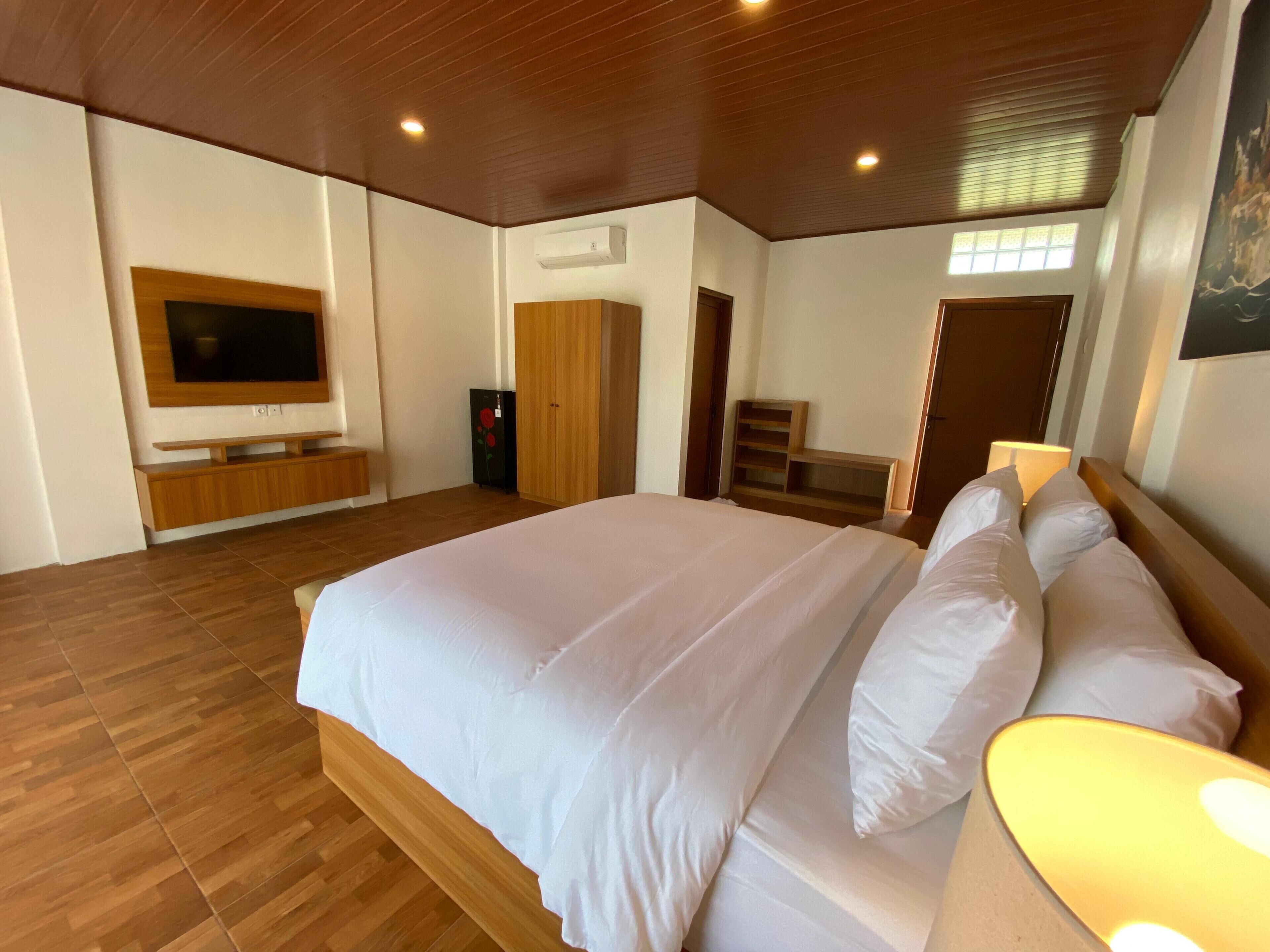A spacious bedroom with a large bed, wooden flooring, a TV mounted on the wall, and a wardrobe.