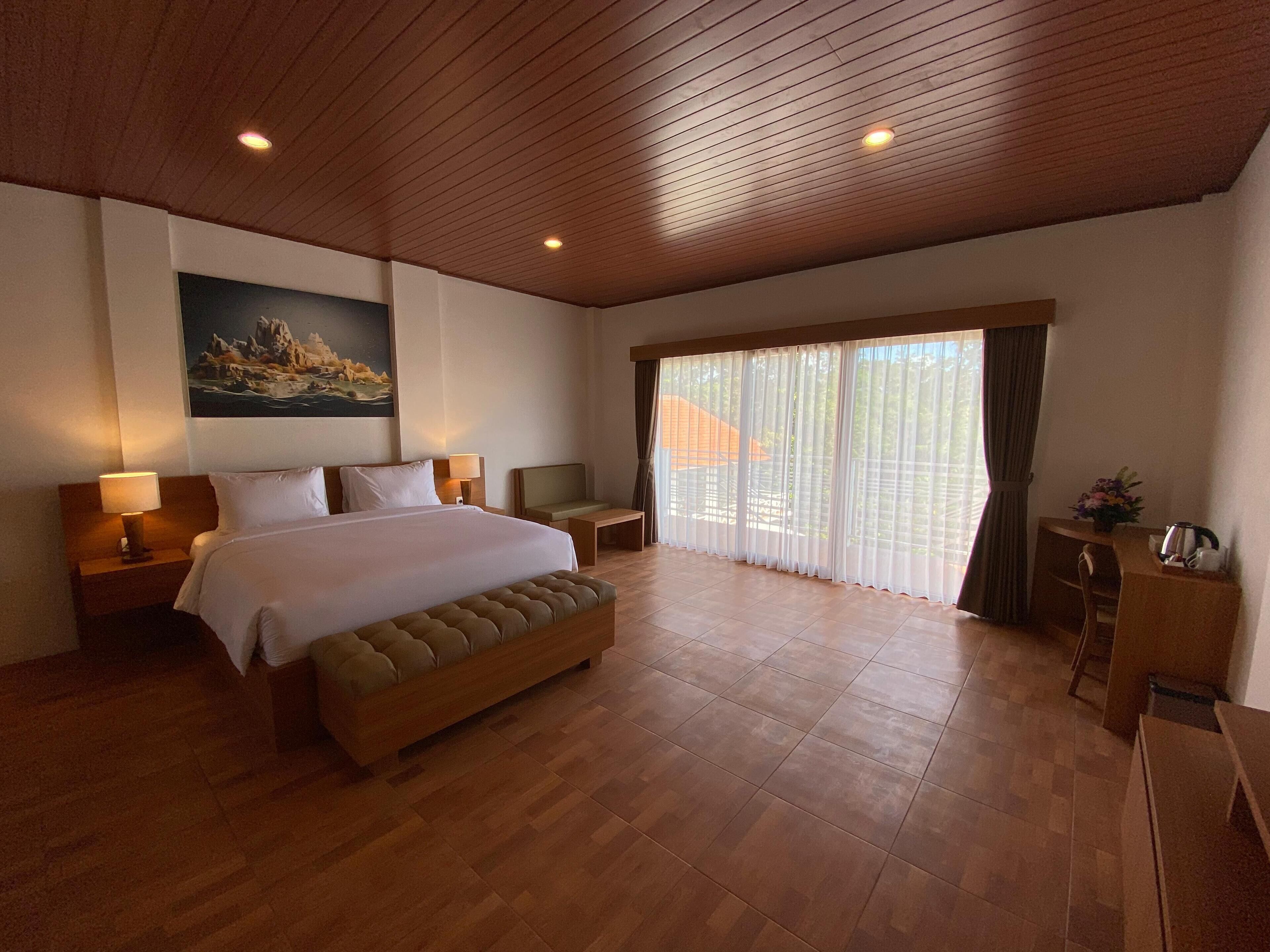 Un dormitorio amplio con una cama grande, cabecero de madera y vistas a un edificio a través de cortinas traslúcidas.