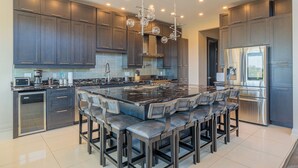 A modern kitchen with dark cabinets, a large island with bar stools, stainless steel appliances, and recessed lighting.