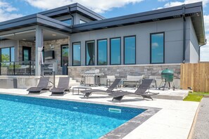 Una casa moderna con piscina, zona de estar exterior y área de barbacoa.