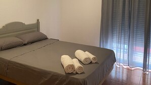 Een enkel bed met een grijze matras en kussens, een plafondventilator en een raam met donkere gordijnen.