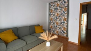 Een woonkamer met een grijze bank, een witte vaas met gedroogde planten, een houten salontafel en een plafondventilator.