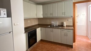Een keuken met witte kastjes, een inbouwoven en een spoelbak.