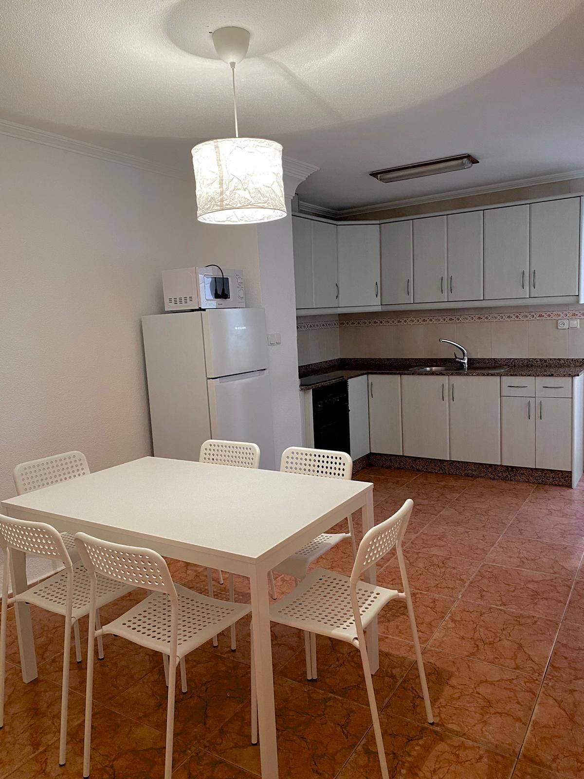 A compact kitchen with white cabinets, a white refrigerator, a sink, and a dining area with a white table and chairs.