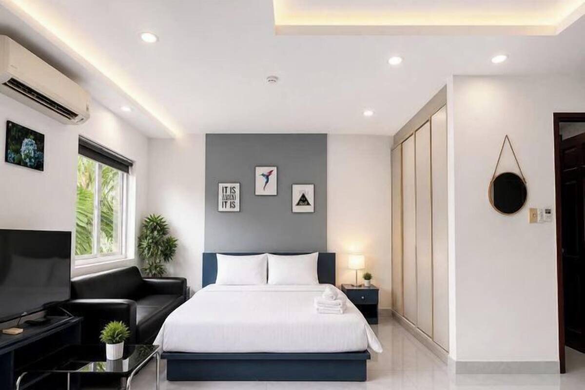 A modern bedroom with a bed, a TV, a desk, and a window.