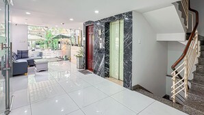 Un hall d'hôtel moderne avec une entrée en verre, un escalier et un espace détente comprenant un canapé et une table basse.