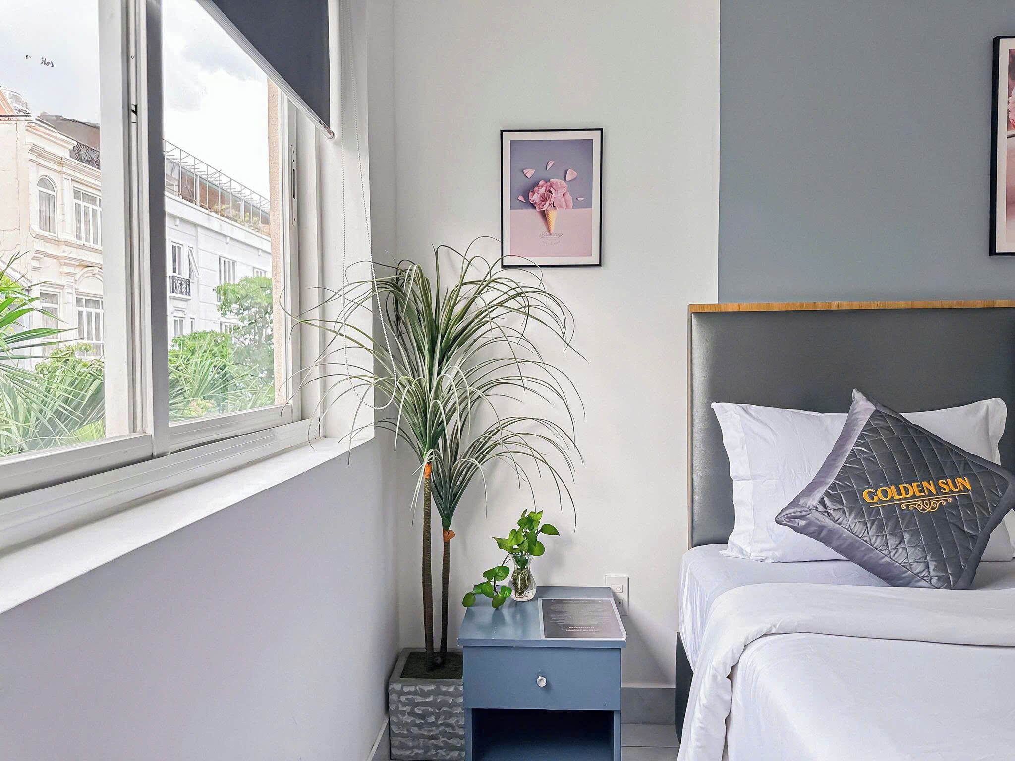 A bedroom with a bed, a nightstand, a potted plant, and a framed picture on the wall.