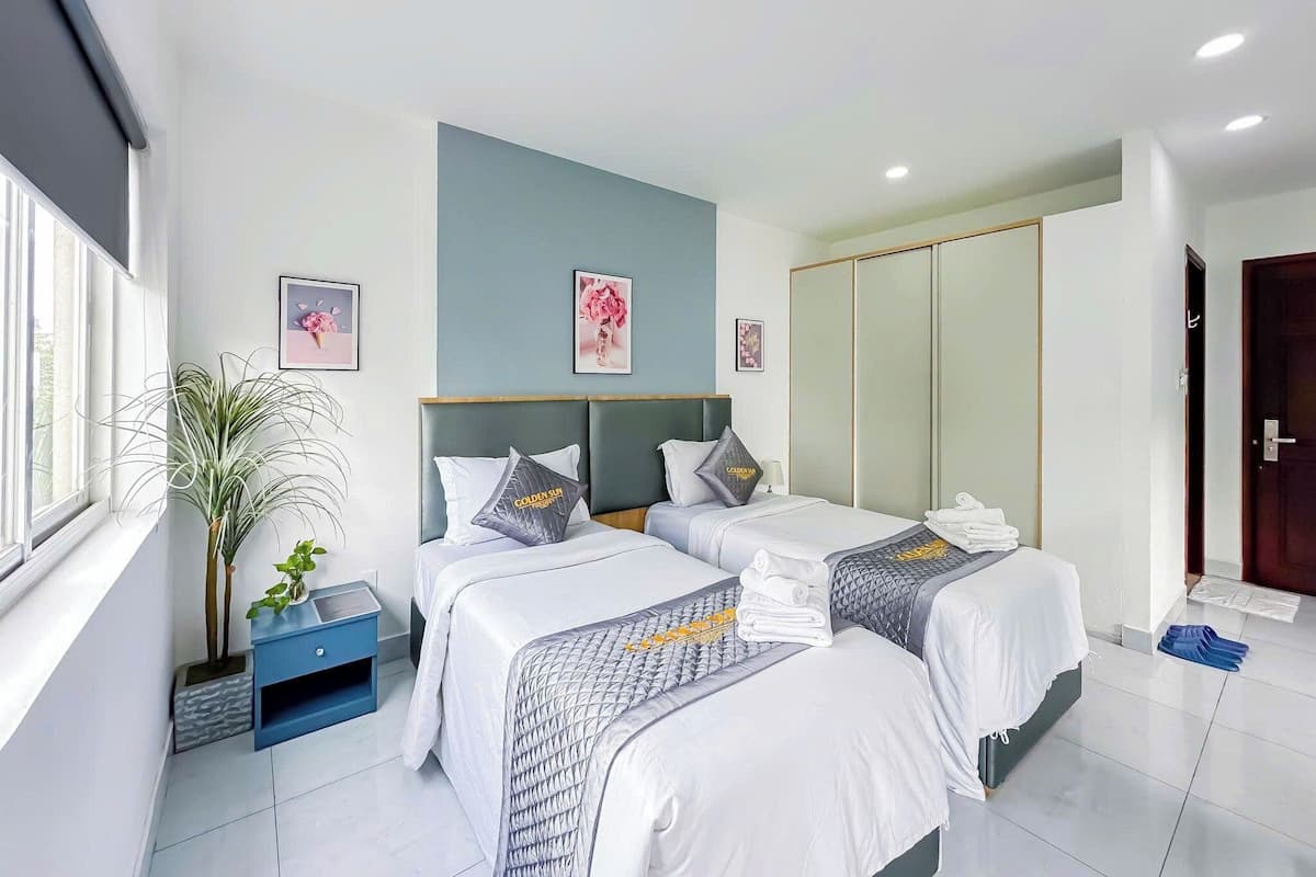 Ein Hotelzimmer mit zwei Betten, einem Blumentopf, einem blauen Nachttisch und einem Kleiderschrank.