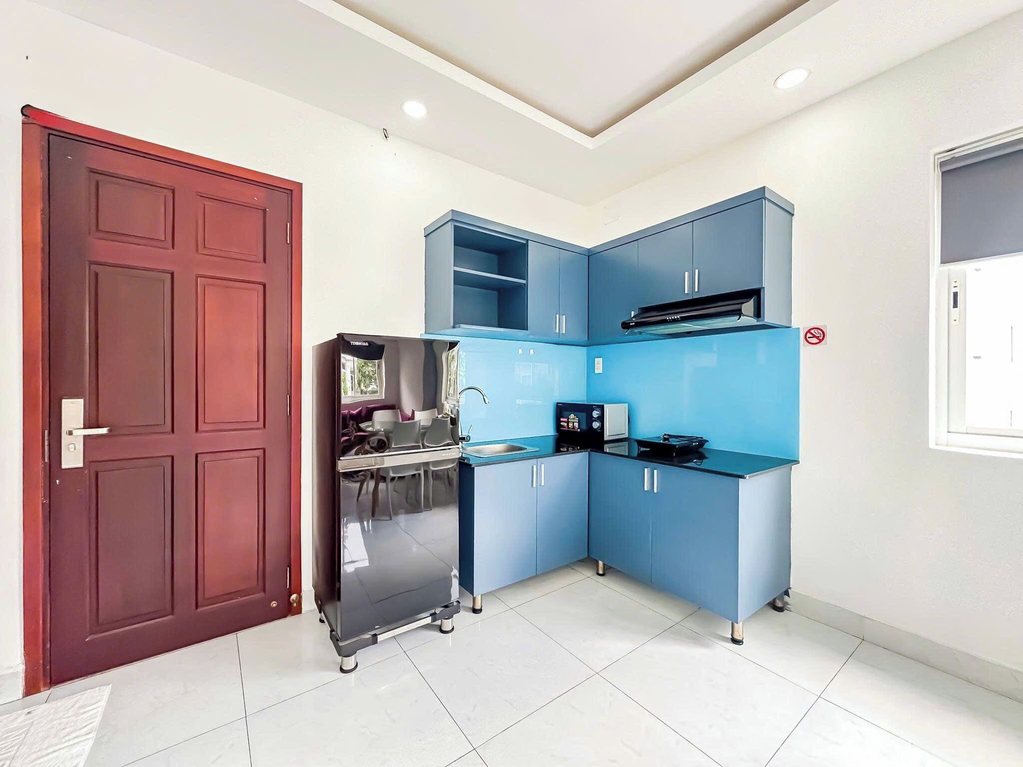 A compact kitchen with blue cabinets, a stainless steel refrigerator, and a built-in oven.