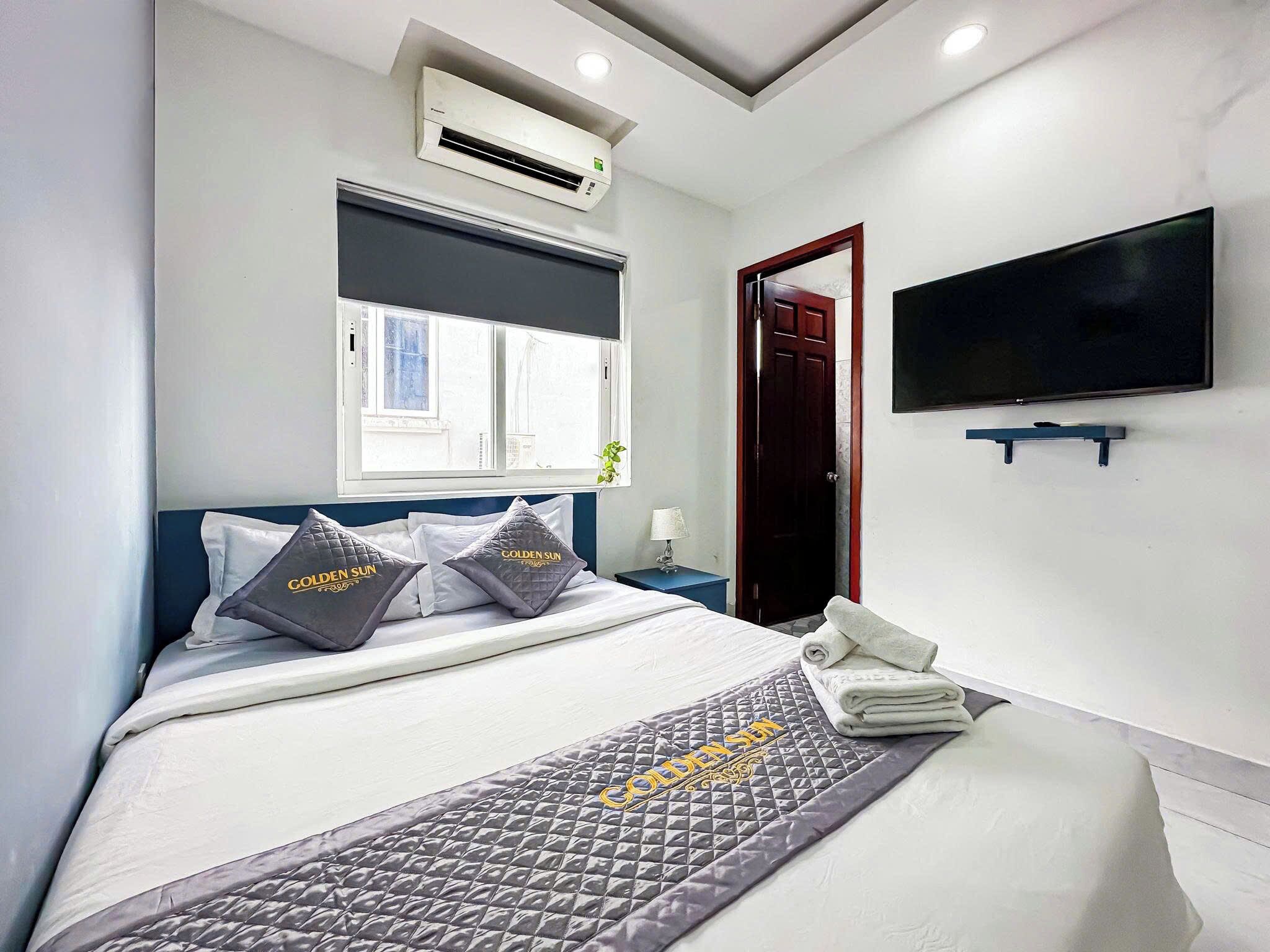 A hotel room with a bed, a TV mounted on the wall, an air conditioning unit, a window, and a door.