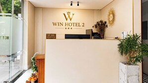 Un comptoir d’accueil avec une enseigne indiquant « WIN HOTEL 2 » et un espace d’accueil agrémenté d’une plante et d’un objet décoratif sur le mur.