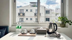 Une pièce dotée d’une grande fenêtre donnant sur un paysage urbain, une table avec une bouilloire, des tasses, une boîte de mouchoirs et une multiprise.