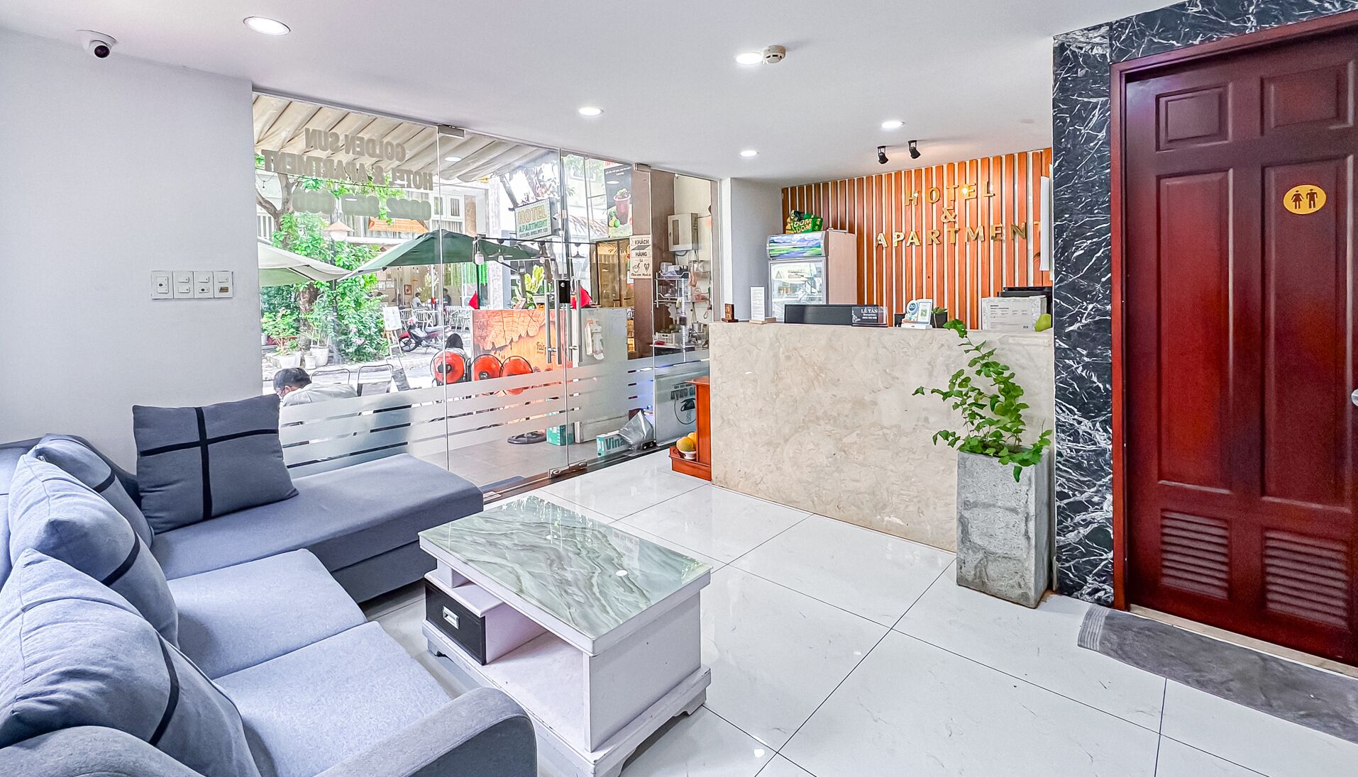 A modern hotel lobby with a reception desk, seating area, and a view of the outdoor area.