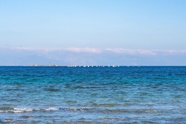 A coastal view with sailboats on the water and a distant shoreline with buildings.