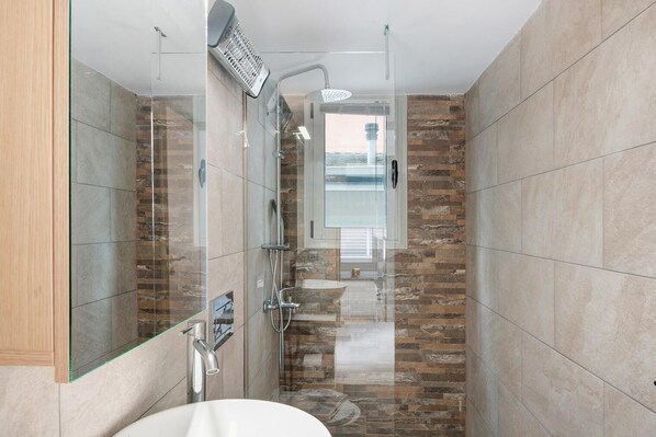 A modern bathroom with a glass-enclosed shower, a white sink, and a stone-tiled shower wall.