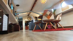 Een moderne woonkamer met een houten vloer, een rood kleed en een grote televisie. Er staan twee stoelen met een geruit patroon en houten poten.