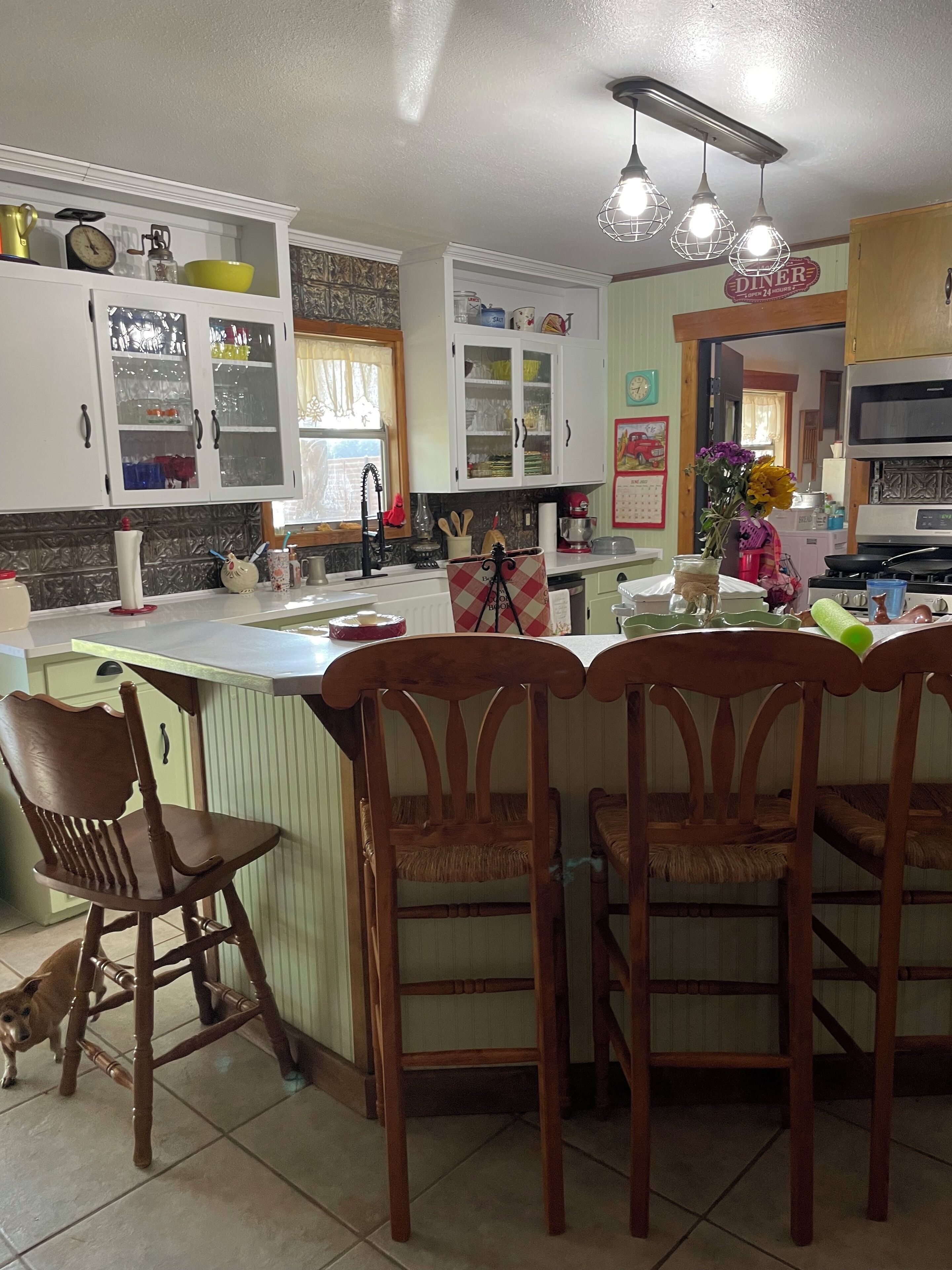 A kitchen with white cabinets, a central island with bar stools, a dog, and various kitchen appliances.