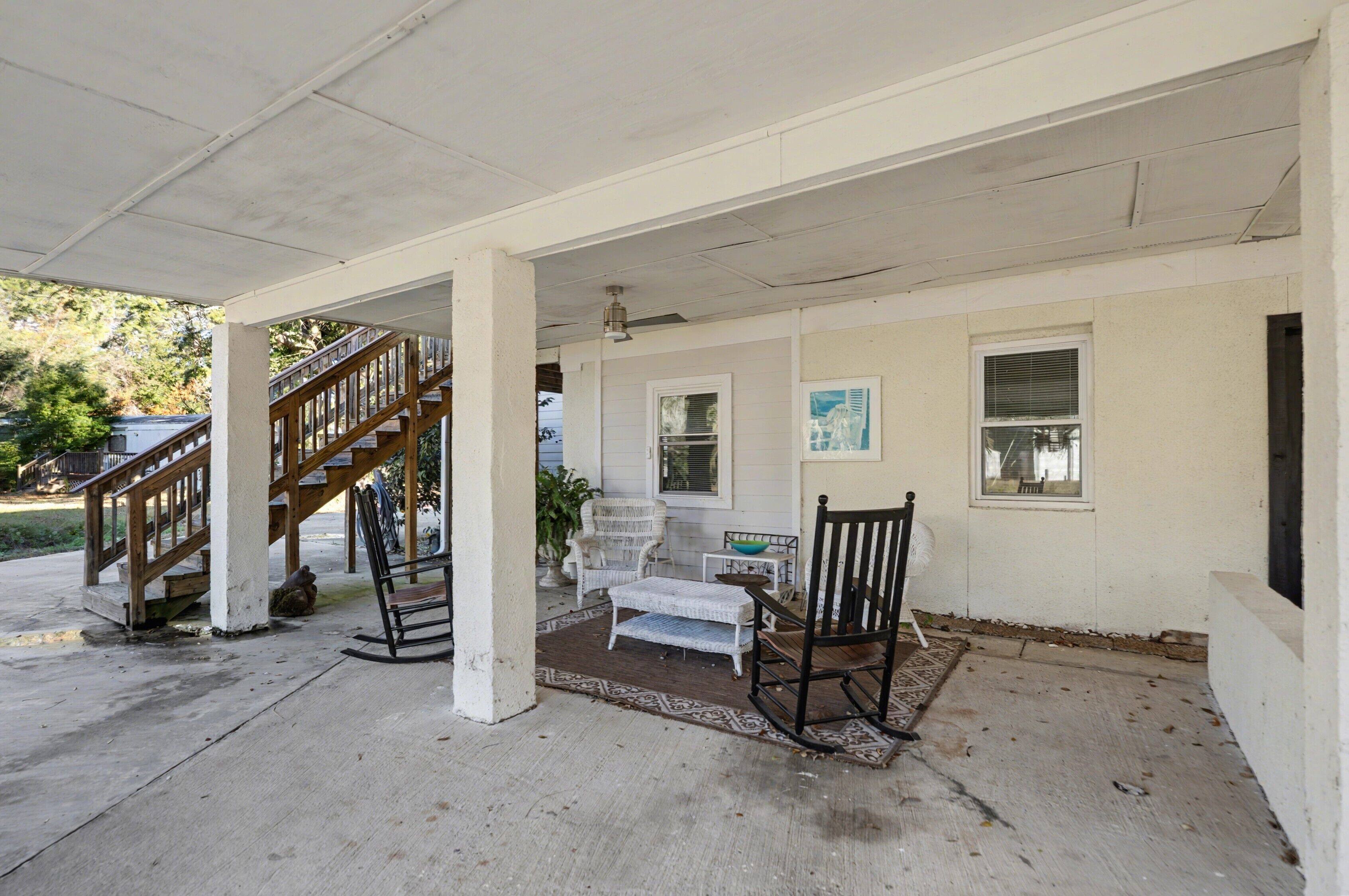 A covered porch with a wooden staircase, a small table, a rocking chair, and a bench.