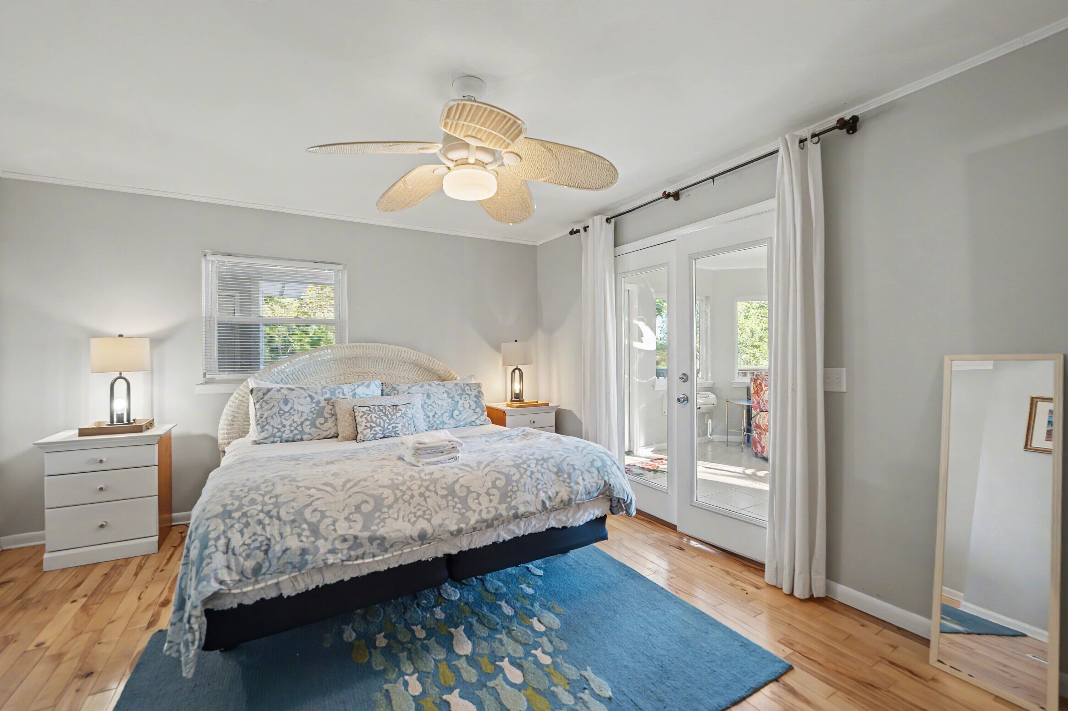 Une chambre à coucher avec un lit, des tables de chevet, un ventilateur de plafond et une grande fenêtre avec des rideaux.