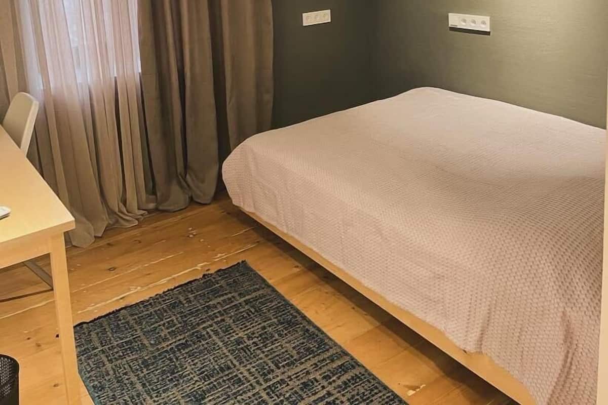 Eine kleine, einfache Unterkunft mit einem Bett, einem Schreibtisch und einem Stuhl.