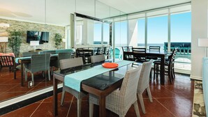 A modern dining area with a glass table, wicker chairs, and a view of the ocean. - 1200 TOP OF EAST BEACH! (Galveston)