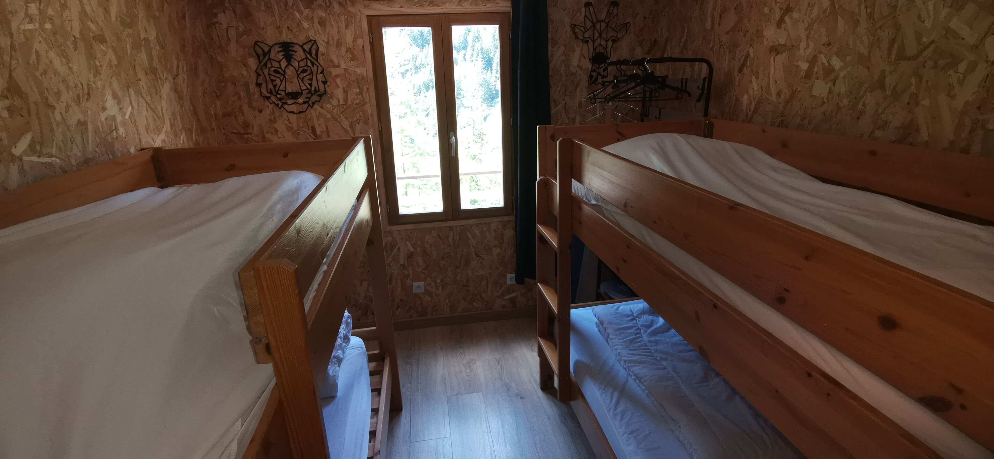 Ein Zimmer mit zwei Holzkaryäten, einem Fenster mit Blick auf Grünflächen und einem an der Wand befestigten Kleiderhaken.