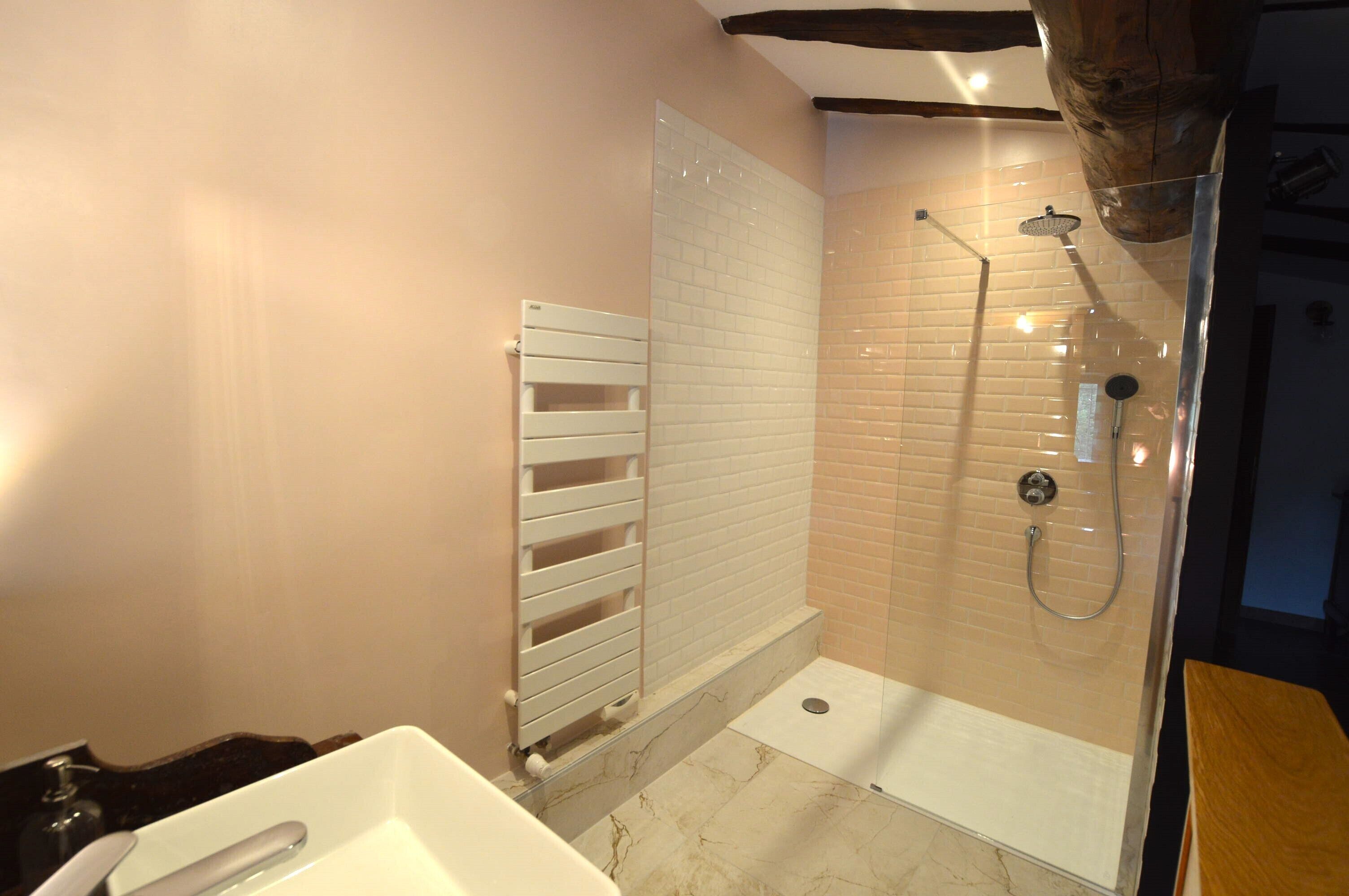 A modern bathroom with a glass-enclosed shower, white tiled walls, and a marble floor.