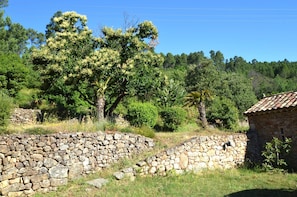 A stone wall with a small stone building, surrounded by lush greenery and trees. - Mas des Druilles (Generargues)