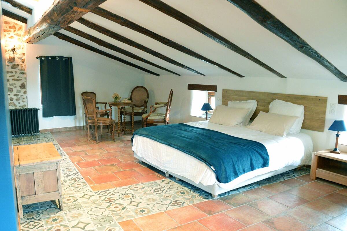 A bedroom with a bed, wooden headboard, a small table with chairs, a lamp, and a radiator.