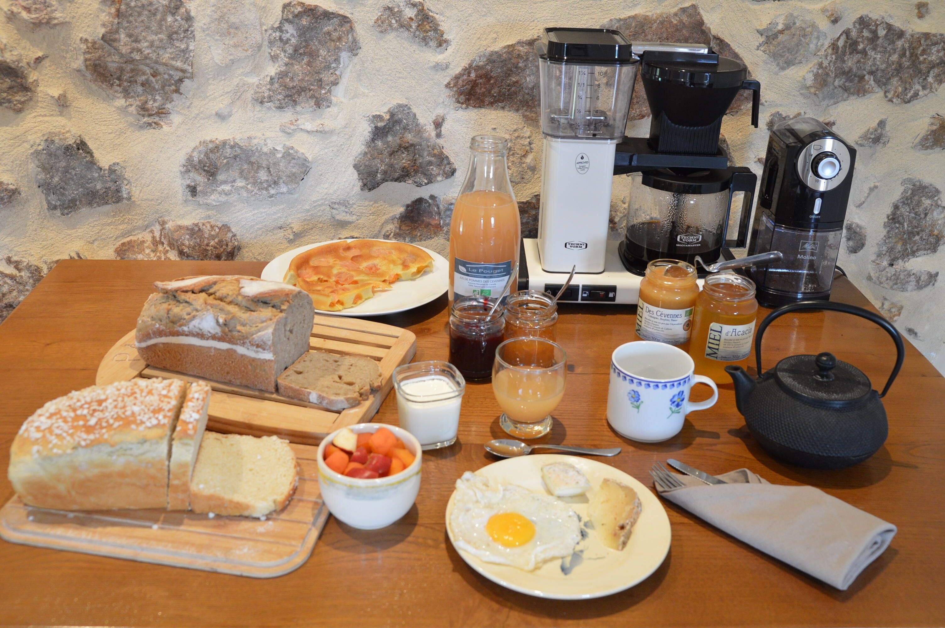 A breakfast table with various food items, a coffee maker, and a teapot.