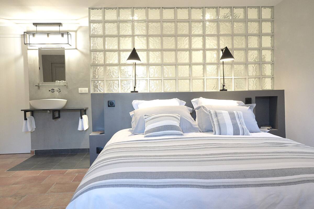 A hotel room with a large bed, a bathroom with a sink, and a frosted glass window.