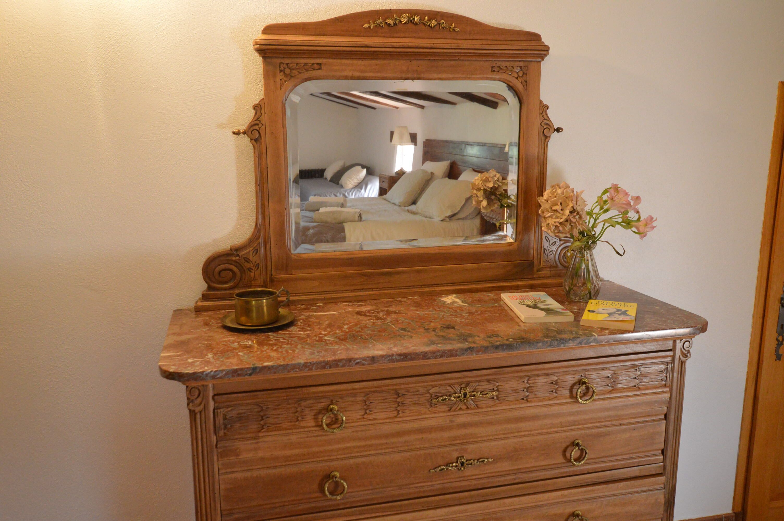 A wooden dresser with a mirror, a vase with flowers, and a small table with a cup and saucer.