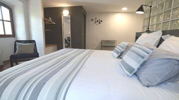 A neatly made bed with striped bedding, a chair with a checkered cushion, and a mirror with a light above it.