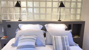 A neatly made bed with white and striped pillows, two black bedside lamps, and a window with frosted glass panes.