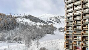 Um edifício alto com várias varandas com vista para uma paisagem coberta de neve, um teleférico e árvores.