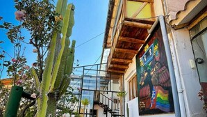 A courtyard with potted cacti, a wooden bench, and a mural on the building wall. - Casa Suecia  (Cusco)