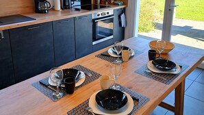 A modern kitchen with dark cabinets, a wooden countertop, and a dining area with a table set for two. - The house at the end of the road  (Poey-d'Oloron)