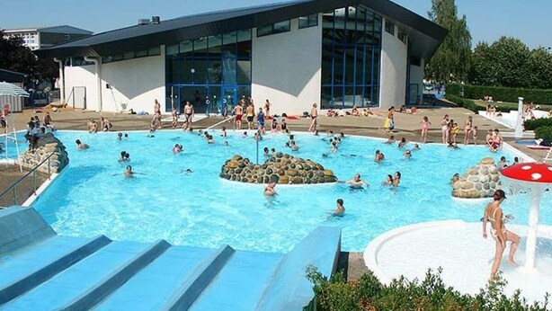 A swimming pool area with multiple pools, a water slide, and a building with large windows. - The house at the end of the road  (Poey-d'Oloron)