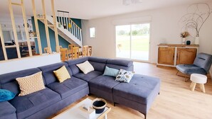 A modern living room with a large sectional sofa, a coffee table, and a dining area with wooden furniture. - The house at the end of the road  (Poey-d'Oloron)