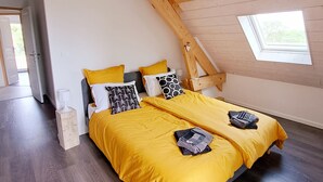 A bedroom with a sloped ceiling, wooden beams, a bed with yellow bedding, and a small window. - The house at the end of the road  (Poey-d'Oloron)