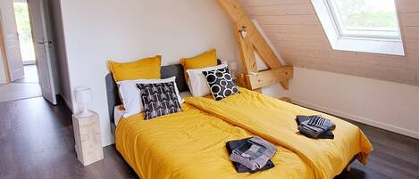 A bedroom with a sloped ceiling, wooden beams, a bed with yellow bedding, and a small window.