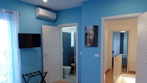 Ein Zimmer mit blauen Wänden, einem angebrachten Fernseher, einer Tür zum Badezimmer und einer Treppe.