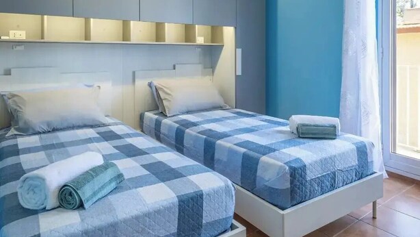 Ein Schlafzimmer mit zwei Betten, einem großen Fenster mit Vorhang und einer blauen Wand.