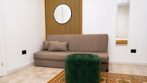 Ein stilvolles Wohnzimmer mit einer Couch, einem Hocker, einem gemusterten Teppich und einem Wandspiegel.