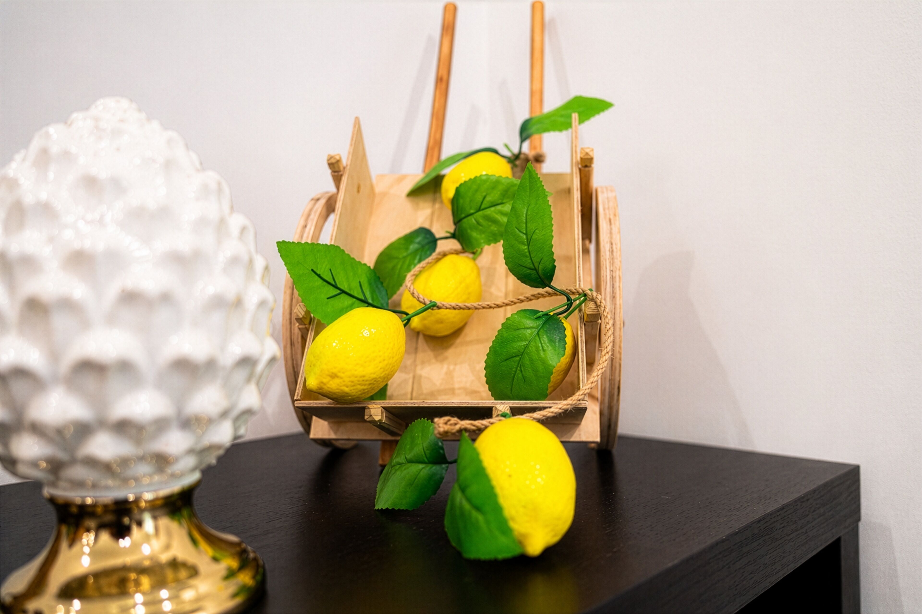 A wooden basket with lemons and green leaves on a dark surface.