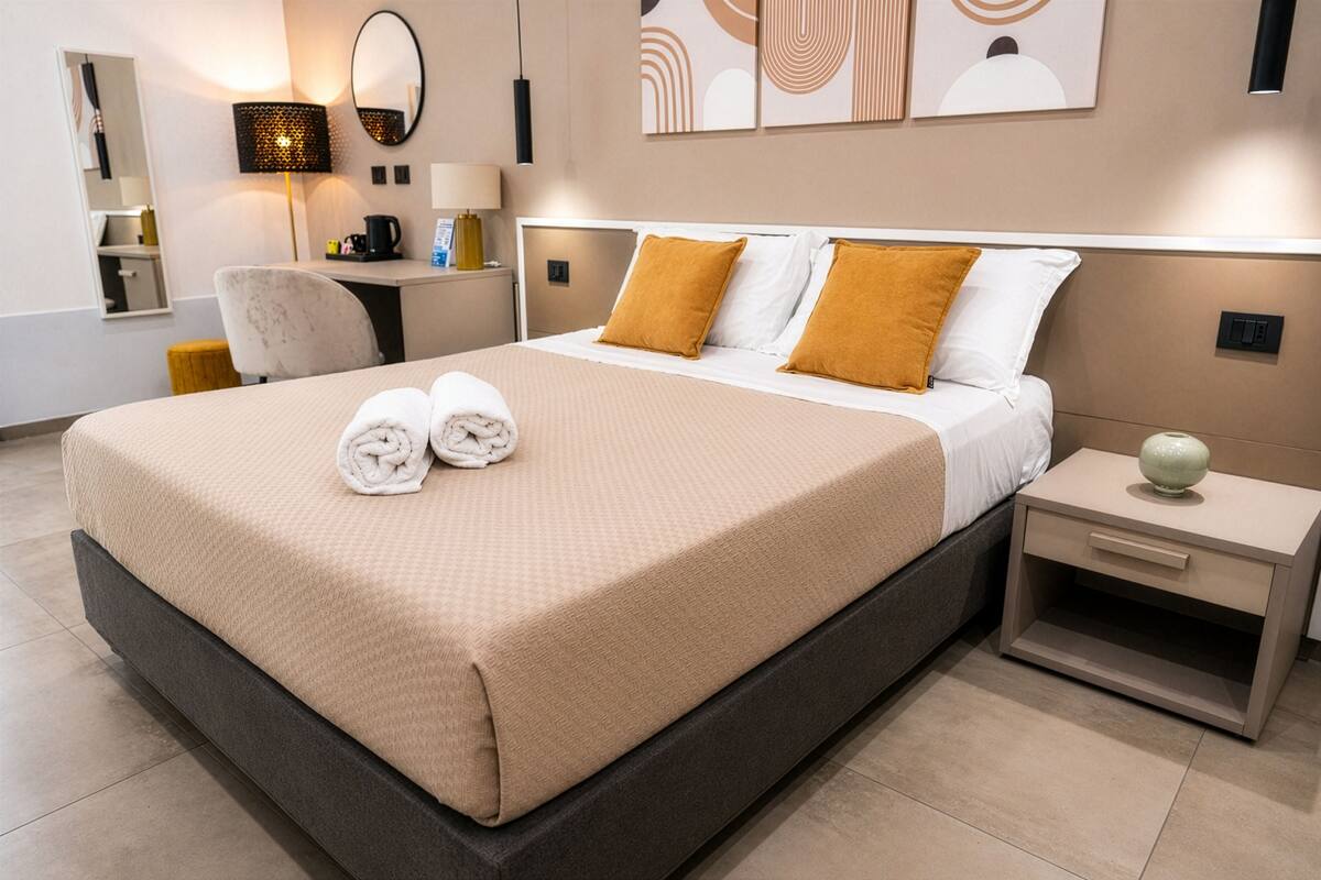 Ein Hotelzimmer mit einem großen Bett, einem Nachttisch, einem Schreibtisch, einem Sessel und einem Spiegel.