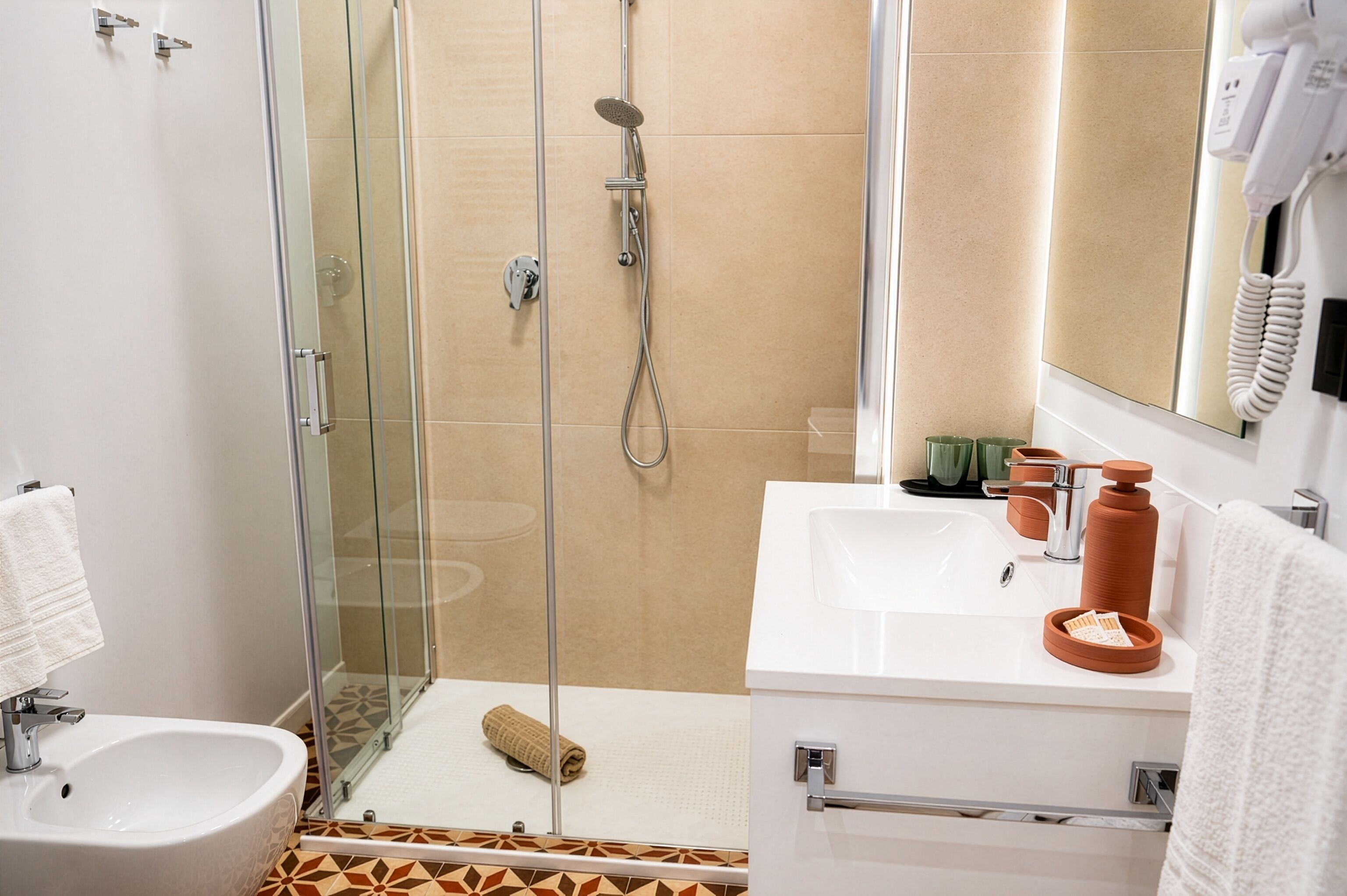 A modern bathroom with a glass-enclosed shower, a white sink, and a mirror with a hairdryer.