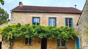 Ein Steinhäuschen mit Ziegeldach, drei Fenster mit blauen Rollläden und einer mit Efeu bewachsenen Vorderseite.