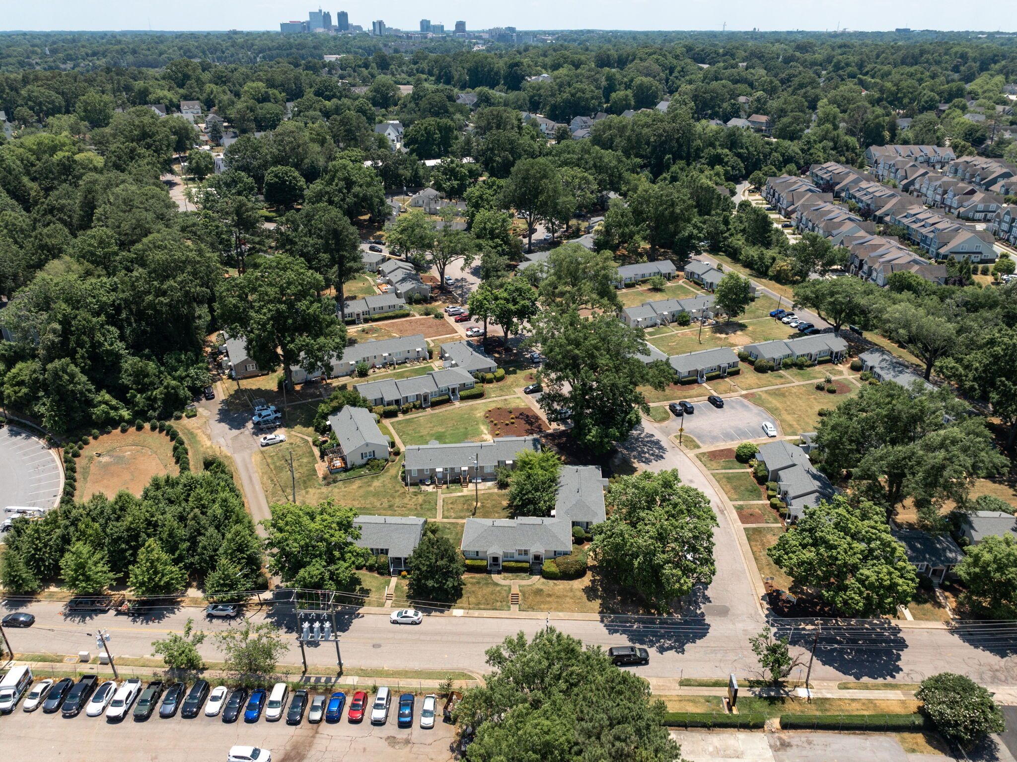 An aerial view of a residential area with detached houses, a parking lot, and a distant city skyline.